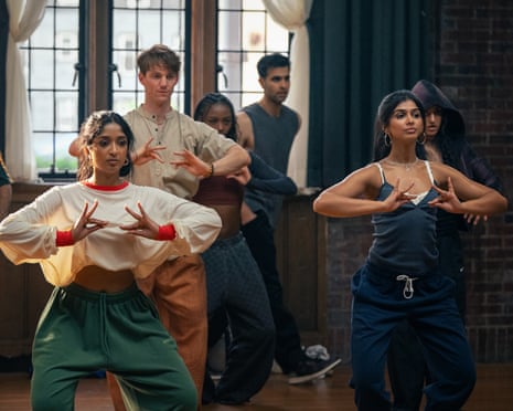 Maya and Sumi lead a group dance move, hands crossed over chests, others following behind
