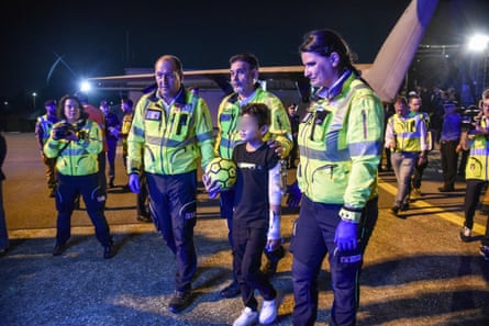 Adam al-Najjar next to a plane holding a football with support workers in high vis jackets