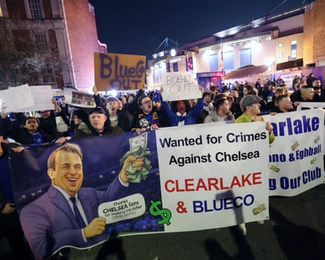 Chelsea fans hold protest signs reading "Boehly Out" outside Stamford Bridge at night
