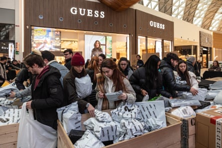 people sift through large bins containing plastic-wrapped “mystery packs” in a shopping mall