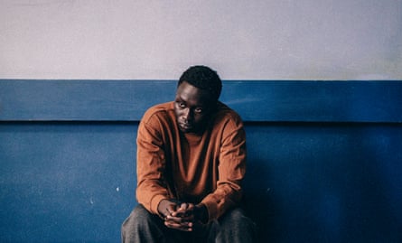 A Black boy sits looking despondent against an institutional wall