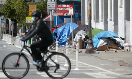 A cyclist rides past a homeless encampment along a sidewalk in San Francisco.