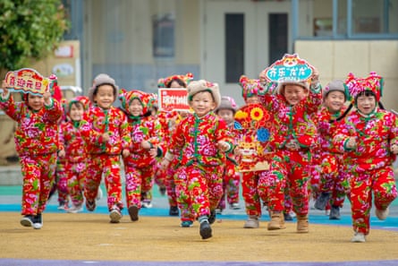 Kindergarten children dressed in traditional floral-print padded coats run towards the camera
