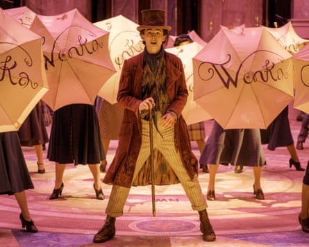 Timothée Chalamet as young Willy Wonka in a brown topcoat, a matching brown top hat, and a colourful polka-dot scarf.