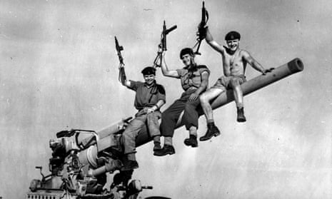 Three British soldiers sit triumphantly on a British-made gun they captured from Egyptian forces during the Suez crisis