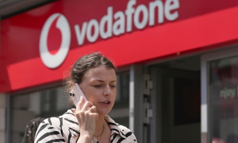 A woman talking on her mobile, walks past a Vodafone store in London, in 2023.
