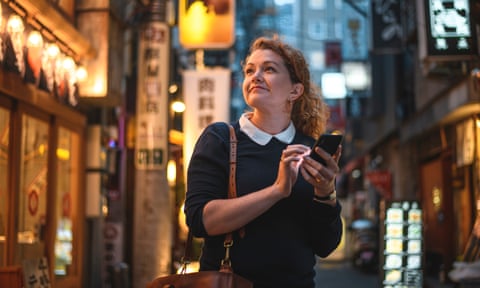 Smiling independent Caucasian woman traveling in Tokyo with the help of her smart phone to navigate sightseeing.