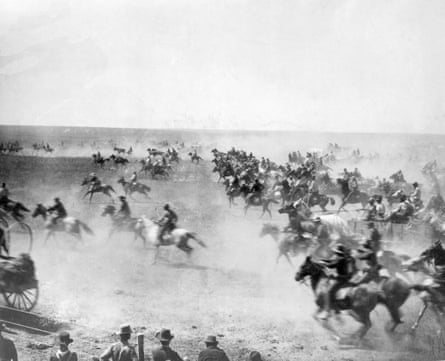 A mob of people on horses race across an open field