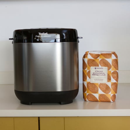 A Tefal stainless steel bread maker stands beside a bag of wholemeal flour on a counter