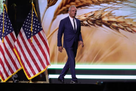 a man in a suit walks on stage, american flags beside him