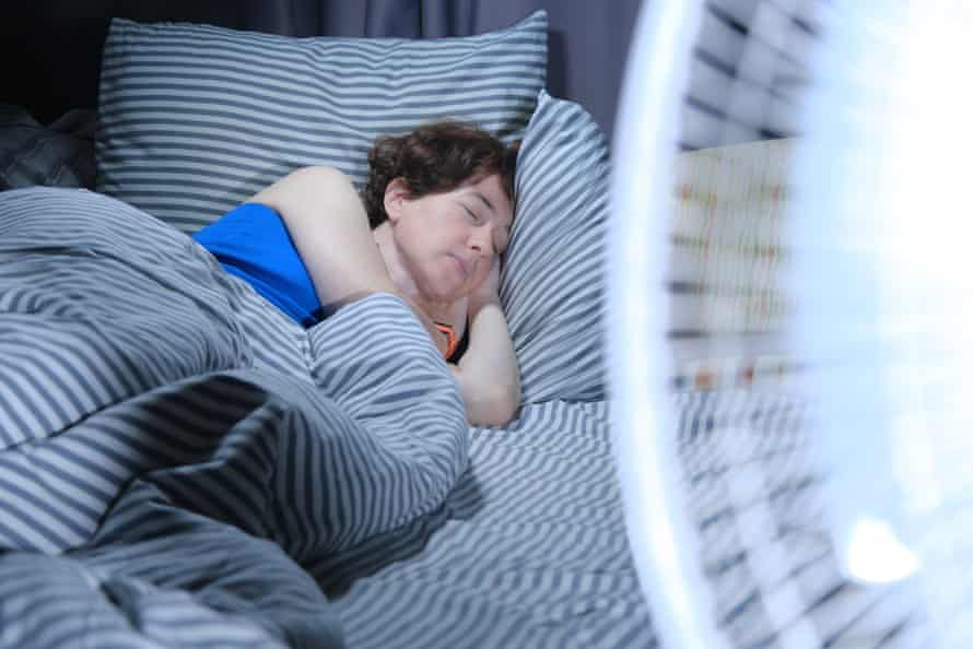 woman sleeping in bed with blowing electric fan in foreground