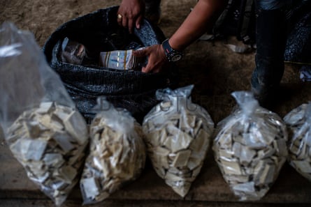 A man pull a bundle of money out of bag next to four plastic bags full of cocoa paste