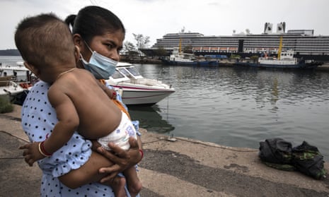 A woman wearing a mask holds her baby on the dock outside the MS Westerdam cruise ship docked in Sihanoukville, Cambodia
