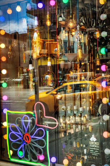 Manhattan, 2017. candy-coloured lights seen through a shop window, a yellow cab seen reflected in the glass