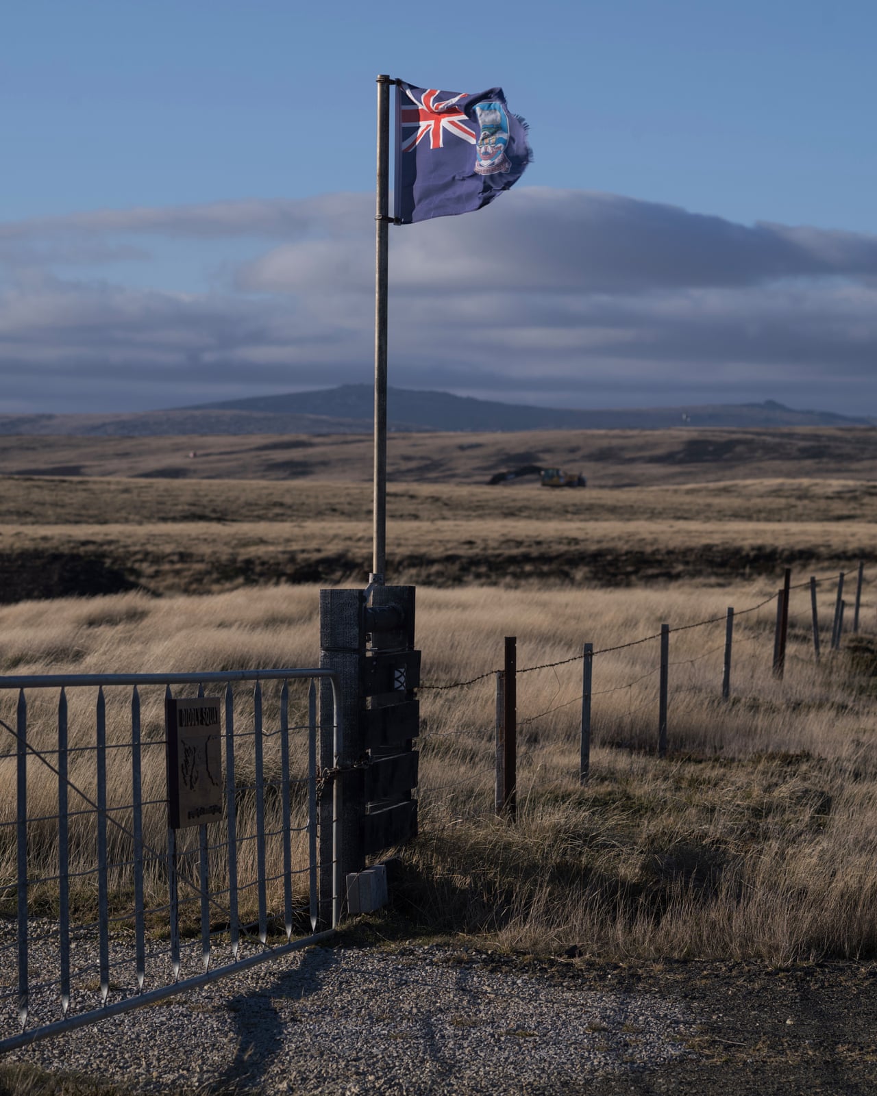 A flag flies beside a gate overlooking the Falkland Islands' windswept grassland and hills
