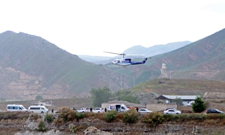 A helicopter takes off above vehicles in a mountainous landscape