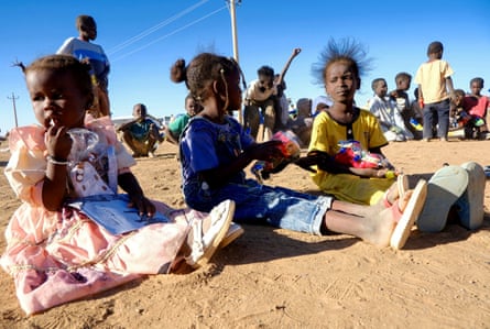 Displaced girls from El Fasher sit on the ground with toys in their hands.
