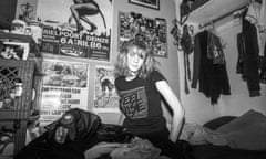 A black and white shot of Ali in her early 20s in her messy bedroom, surrounded by clothes, posters and photos