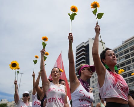 Women marching in a row on a street with slogans written on their T-shirts hold up sunflowers