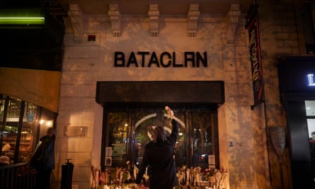 A person attending a memorial on the anniversary of the attack holds up a flower towards a concert hall