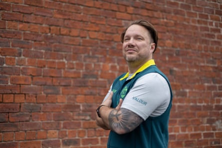 Wearing his Team Australia top, Pike stands with his arms folded against a brick wall, smiling softly