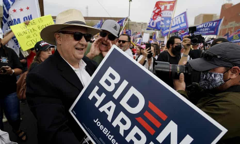 A man in a cowboy hat carrying a Biden/Harris sign is heckled by a Trump supporter