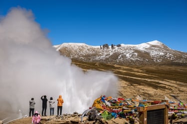 People wearing waterproofs watch as water is fired into the air above them