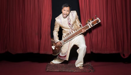 Rhik Samadder pretending to play a sitar in front of red theatre curtains
