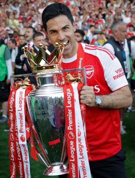 Mikel Arteta the Arsenal manager bites the top of the trophy in celebration after winning the Premier League.