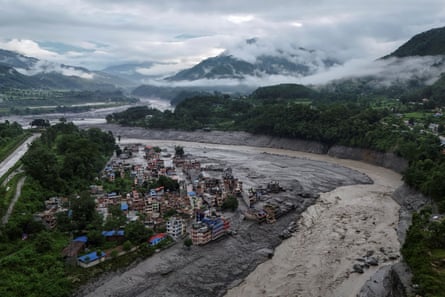 An aerial view of a town covered in heavy mud caused by flooding, with mountains in the background