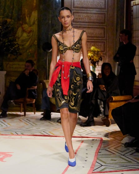 A Versace model on the catwalk in a matching bra and skirt with a red jumper tied around her waist.