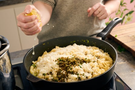 A pan full of pasta and cheese, with a hand squeezing a lemon with juice dripping into the pan. 