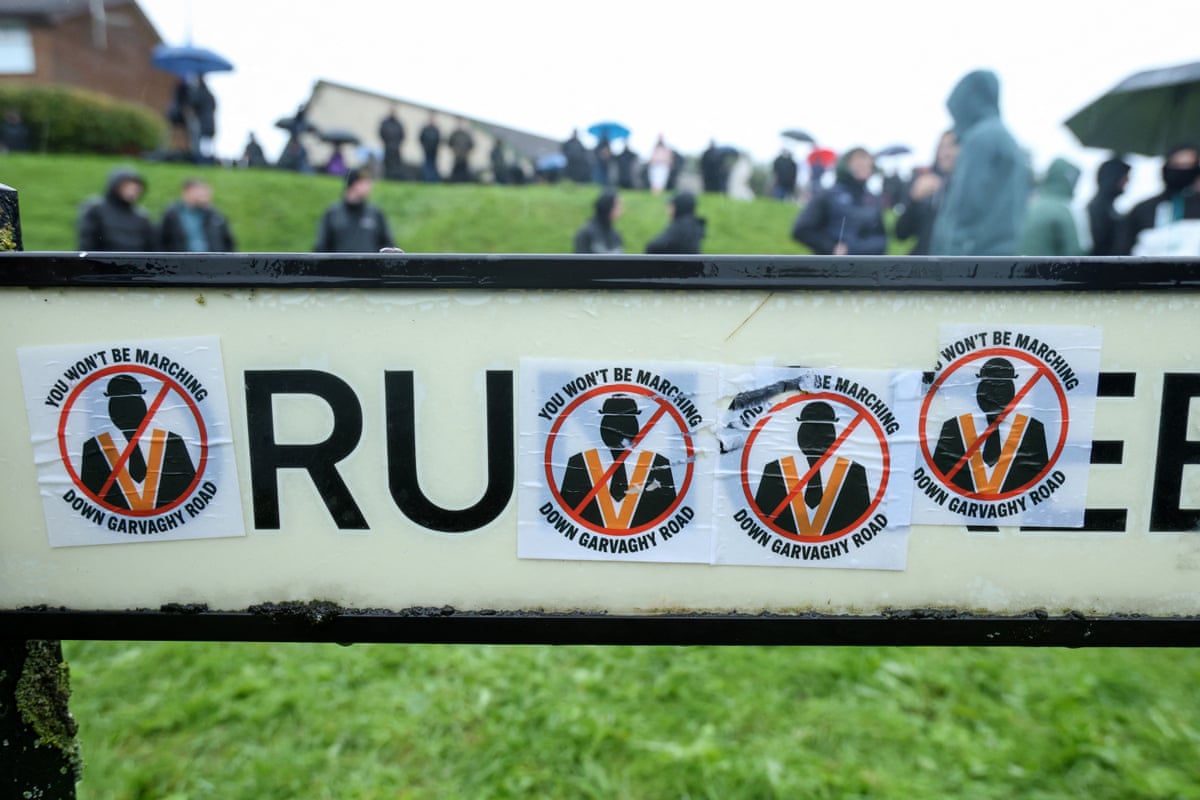 Stickers cover a road sign as a crowd of protesters gather to block the Garvaghy Road in Portadown, Northern Ireland in the morning of September 27, 2026, to prevent a parade of marchers from the Orange Order using the route through the mainly nationalist area of the town.