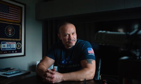 a man wearing a shirt with a US flag on the sleeve sits with his hands folded on a table