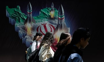 Iranian women walk past a banner showing missiles being launched from Iran
