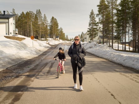 Woman walking down road with child on bicycle 