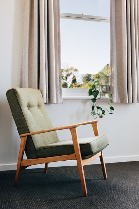 Une chaise longue vert olive près d'une fenêtre encadrée de rideaux gris