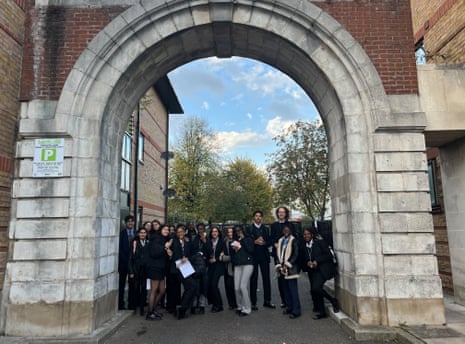 Young people in school uniform pose beneath the arch