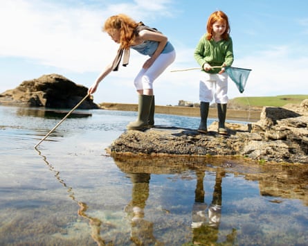 Two girls fishing in a rock pool in Cornwall, UK
