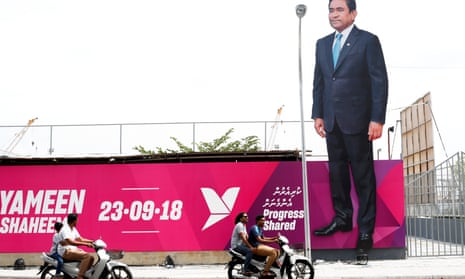 People ride motorcycles past an image of Maldives President Abdulla Yameen