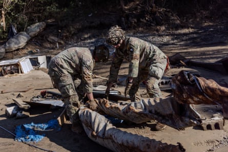 Two people in camouflage uniformas drag a large twisted pipe.
