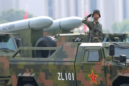 A soldier salutes while riding on the back of a military truck