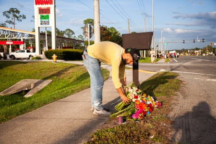 A man bends down and places flowers on a sidewalk next to other bouquets