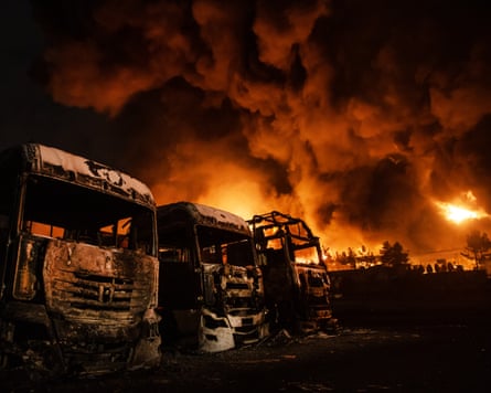 Fire raging at an oil depot with burnt-out trucks in the foreground.
