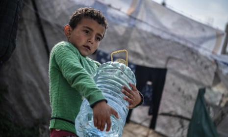 A child carries fresh water in a plastic bottle as Palestinians who fled from Israeli attacks and took refuge in Rafah city continue their daily lives in makeshift tents with limited means.