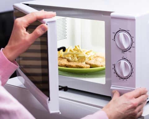 A woman putting a plate of food into a microwave.