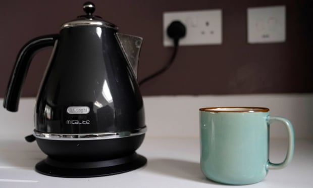 A DeLonghi kettle plugged in next to a cup of coffee in a kitchen