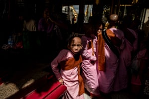 A girl wearing a pink nun’s habit looks out of shadows into the camera