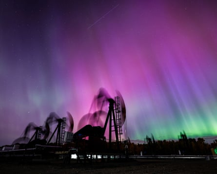 Aurora borealis glows pink and green above silhouetted oil pump jacks in Alberta