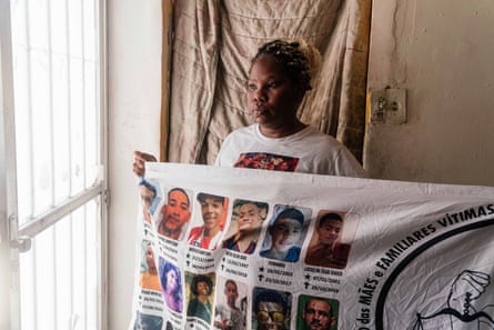A woman stands by a window holding a banner with photographs of people on it